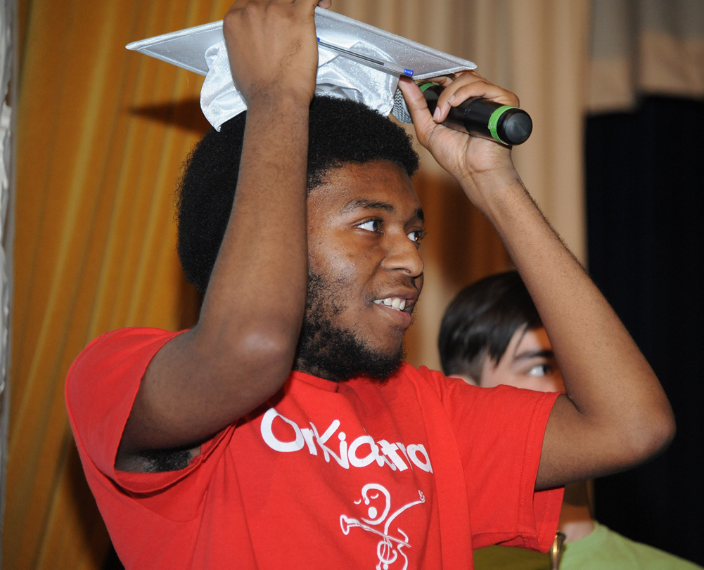 A young man holds a graduation cap. He is smiling.