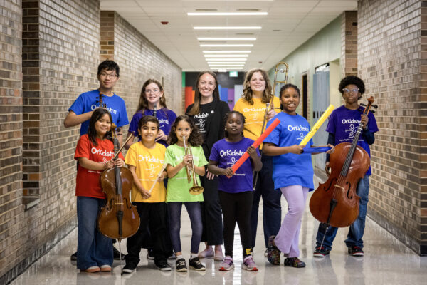 Ms. Danielle Girard, the new Artistic Managing Director at OrKidstra, is surrounded by participating students with their instruments.